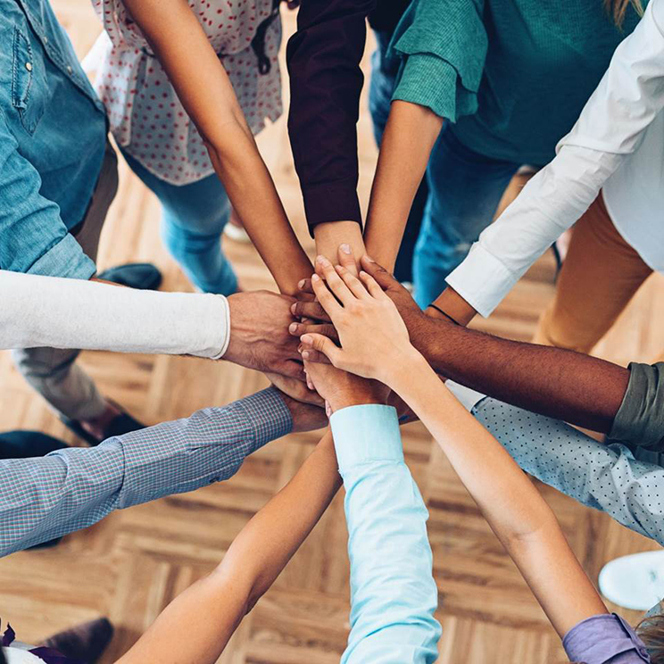 people in a circle with hands stacked 'go team' fashion in the center