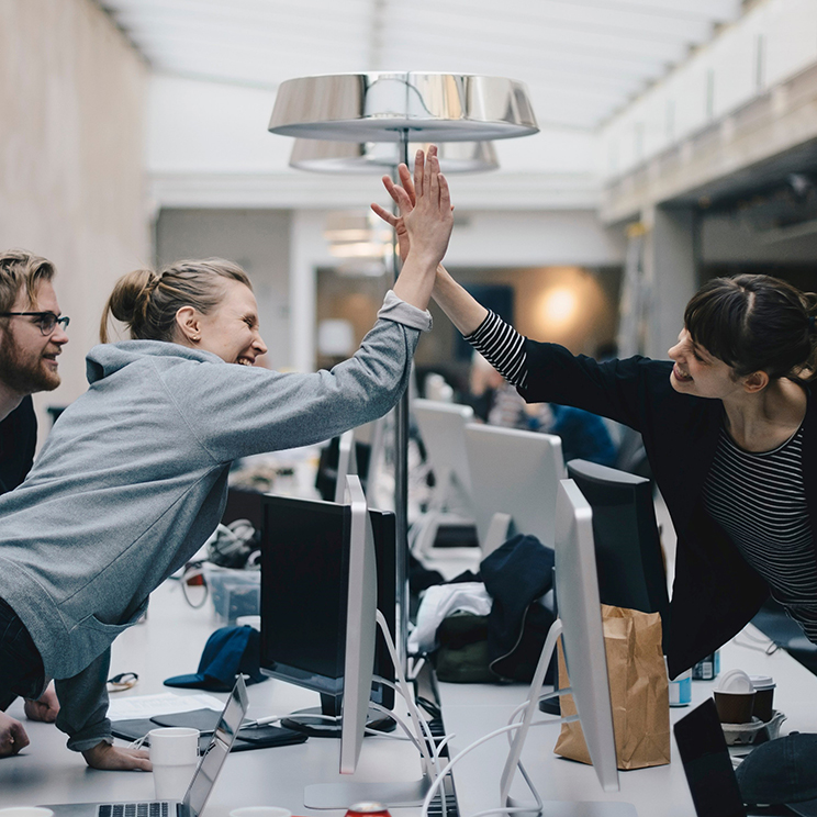 Two business women hi-fiving over a desk with computers on it