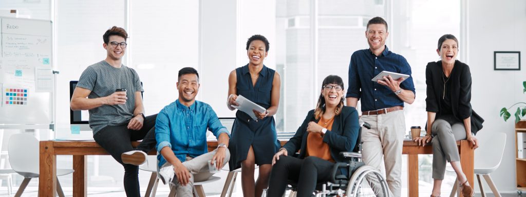 People in an office, smiling, with different genders, abilities, and ethnicities